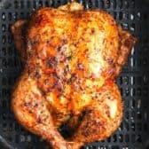 a cooked whole chicken in an air fryer basket