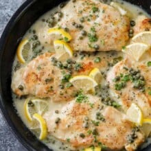 a skillet of chicken piccata garnished with lemon slices
