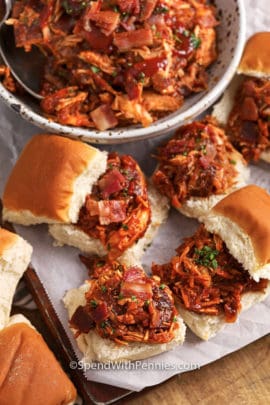BBQ chicken sliders on parchment paper with the bowl of meat on the side