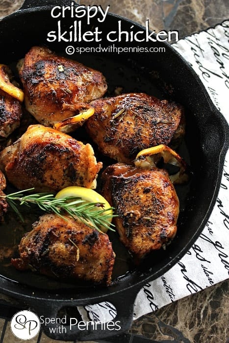 aCrispy Skillet Chicken with crispy skin, roasted lemons and rosemary garnish in a skillet