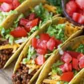 Ground beef tacos in a row on a wooden board