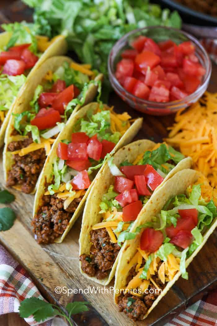 Ground beef tacos on a wooden board with cheese tomatoes and lettuce on the side