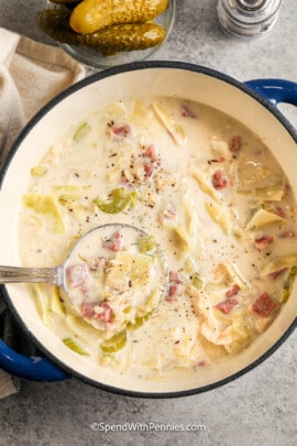 a pot of reuben soup with a ladle in it next to pickles