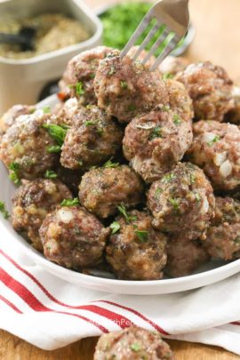 Taking a meatball off a plate of them with a fork